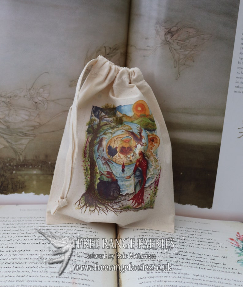 May include: A white cotton drawstring bag with a colorful illustration of a fairy scene. The illustration features a tree, a cauldron, a red-robed figure, and a sun. The bag is printed with the text "Free Range Fairies" and "artwork by Kate Monkman".