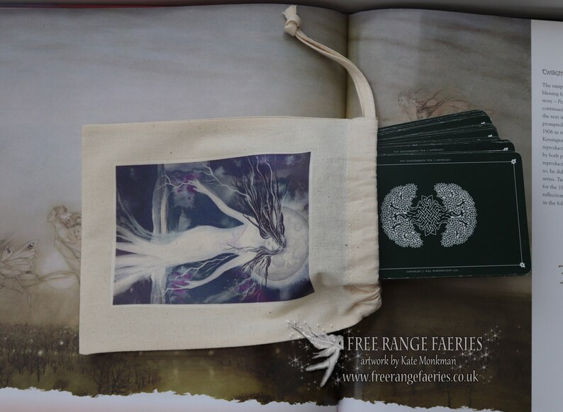 Puede incluir: Una bolsa de lona blanca con cierre de cord&oacute;n. La bolsa tiene una imagen impresa de un hada con el pelo largo y suelto y una luna en el fondo. La bolsa est&aacute; llena de una baraja de cartas con fondo verde y un dise&ntilde;o de &aacute;rbol blanco. El texto "FREE RANGE FAERIES artwork by Kate Monkman www.freerangefaeries.co.uk" est&aacute; impreso en la parte inferior de la imagen.