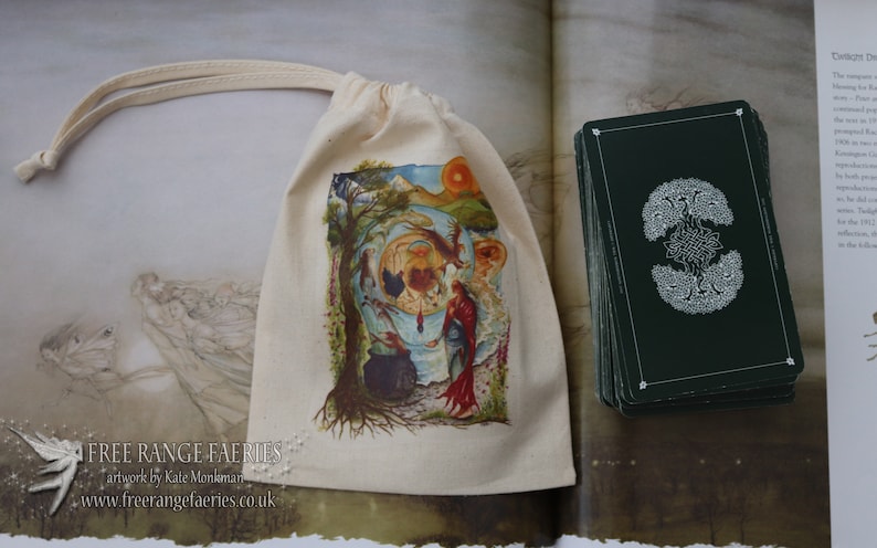 May include: A white canvas bag with a drawstring closure. The bag features a colorful illustration of a woman standing in a forest with a cauldron and a tree. The bag has the text "FREE RANGE FAERIES" printed on the front. The bag is sitting on top of a book with a deck of cards.