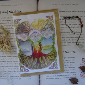 May include: A watercolor painting of a tree with rainbow colored rings around the trunk. The tree has large wings and is surrounded by a mountain range and a body of water. The painting is on a card with a Celtic knot border.