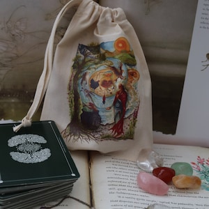 May include: A small, white drawstring bag with a colorful illustration of a tree and a woman. The bag is sitting on a book with a stack of green cards and a necklace with colorful beads. The book has text that reads "But usually people part of the Land Forest. Kee turned his green not like others within walk in at once in bet "How may that be astonished. For informed me of the notice that the air in still, quiet, almost breathey that characterizes the air the Subterranean realm. "It is really quite simple," replied Kee patiently. "There the that disguises our world is nature of all green"