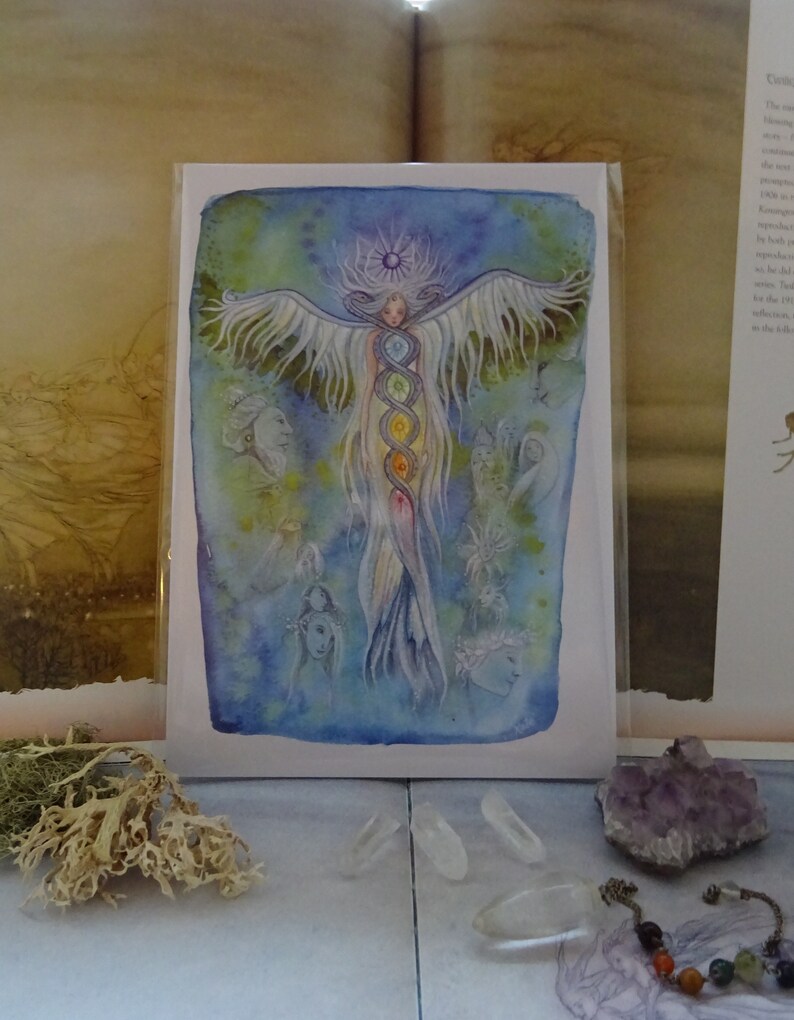 May include: A watercolor painting of a woman with wings and a rainbow aura. The woman is surrounded by smaller figures and flowers. The painting is on a white card with a blue border.