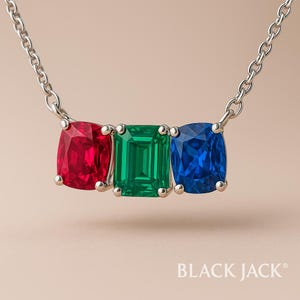 May include: Silver necklace with three gemstones: a red cushion-cut ruby, a green emerald-cut emerald, and a blue cushion-cut sapphire. The gemstones are set in silver and suspended from a delicate silver chain. The brand name "BLACK JACK" is at the bottom.