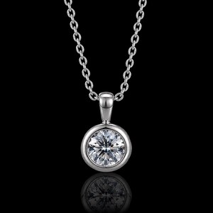 Puede incluir: Un collar de tono plateado con una piedra redonda transparente de talla brillante engastada en un bisel liso y pulido. El colgante cuelga de una cadena fina a juego con eslabones ovalados pequeños y uniformes sobre un fondo negro.