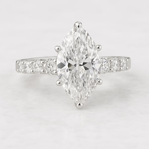 May include: A marquise-cut diamond engagement ring. The large, clear diamond is the focal point, set with six prongs. The band features smaller, round diamonds. The ring is set in a white metal, likely platinum or white gold.