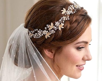 May include: A gold-toned hair vine featuring delicate metal leaves and small clear crystals arranged in a floral pattern. The accessory is worn across the head and is paired with a sheer white veil decorated with tiny scattered white pearls.
