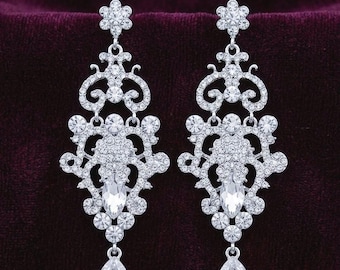 May include: A pair of silver-toned chandelier earrings featuring a floral stud top, an intricate filigree frame encrusted with numerous small clear round crystals, a central marquise-cut crystal, and a dangling pear-shaped crystal drop at the base.