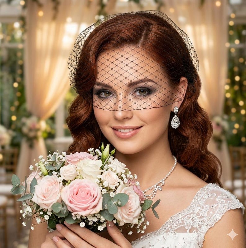 May include: A woman wearing a black net veil, pearl necklace, and diamond earrings, holding a bouquet of pink and white roses. The bouquet includes greenery and baby's breath. She is wearing a white lace dress.
