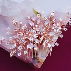 May include: A rose gold hair comb with floral and leaf detailing. The comb features clear and pink crystals, small white beads, and delicate metal leaves. Ideal for weddings or special occasions.