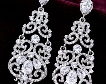 May include: A pair of silver-toned chandelier earrings featuring intricate filigree metalwork encrusted with numerous small clear round stones and accented with larger pear-shaped clear stones at the base and top of each earring.