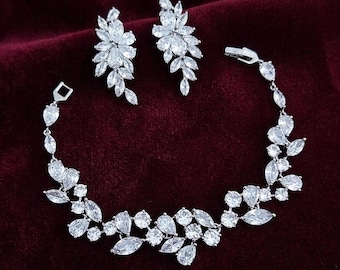 May include: A silver-toned jewelry set consisting of a bracelet and a pair of earrings. Each piece features clear, marquise-cut and round-cut stones arranged in a floral, leaf-like pattern. The bracelet includes a secure metal clasp closure.