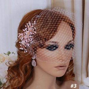 May include: A bridal headpiece featuring a rose gold floral hair comb with clear crystals and a delicate birdcage veil. The comb is adorned with sparkling crystals and small white beads. The image shows a close-up of the headpiece and veil.