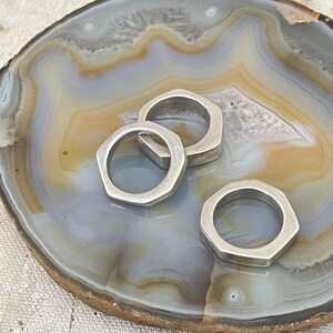 Könnte beinhalten: Drei silberne sechseckige Ringe auf einer hellgrauen und braunen Achat-Schale.