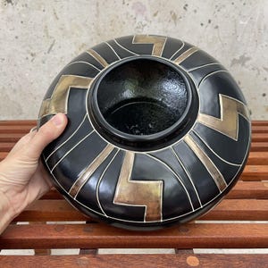 May include: Black ceramic vase with gold geometric designs. The vase has a wide, round opening and a smooth, glossy finish.