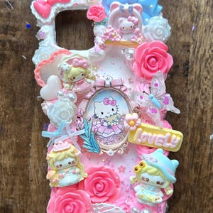 May include: A pink phone case decorated with Hello Kitty and other cartoon characters, pink roses, bows, and the word "LOVELY". The case has a white border and is covered in glitter.
