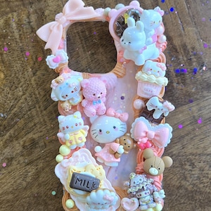 May include: A pink phone case adorned with numerous decorative elements. The case features a variety of small, colorful figurines, including Hello Kitty, teddy bears, cupcakes, and bows. The word "MILK" is visible on a small sign. The overall design is cute and whimsical.