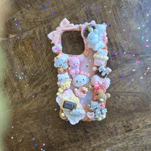 May include: A pink phone case decorated with various 3D elements, including bows, teddy bears, cupcakes, and the text "MILK". The case features a variety of cute characters and is designed with a playful aesthetic.