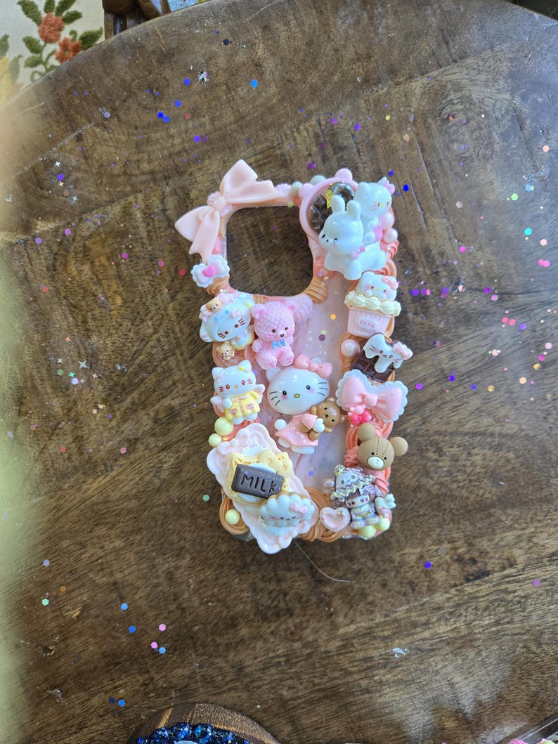 May include: A pink phone case decorated with various 3D elements, including bows, teddy bears, cupcakes, and the text "MILK". The case features a variety of cute characters and is designed with a playful aesthetic.