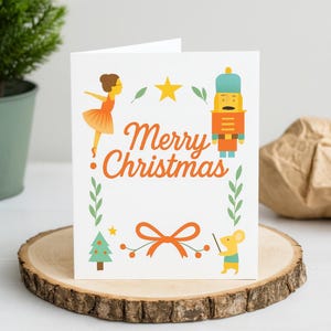 Könnte beinhalten: Eine weiße Weihnachtskarte mit dem Schriftzug "Merry Christmas" in orangefarbener Schrift. Die Karte zeigt Illustrationen einer Ballerina, eines Nussknackers, eines Weihnachtsbaums, einer Schleife und einer Maus. Die Karte liegt auf einer Holzscheibe.