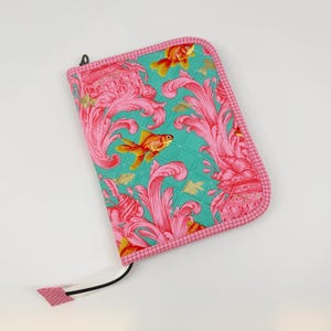 May include: A rectangular quilted fabric case with a zipper closure, featuring a vibrant teal background patterned with bright pink swirling acanthus leaf designs and orange goldfish. The edges are finished with a pink and white grid-patterned trim.