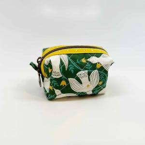 May include: A small, quilted fabric pouch featuring a dark green background with a white bird and yellow flower pattern. The pouch has a yellow zipper closure with white polka dots and a metal zipper pull, showcasing a structured, boxy shape.