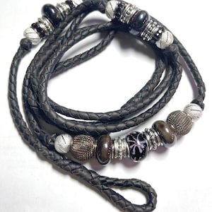 May include: A brown leather cord with silver and black beads. The cord is braided and has a loop at one end.