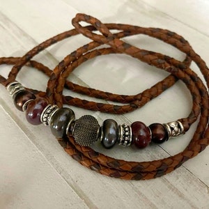 May include: A brown leather cord necklace with a braided design and multiple brown and silver beads.