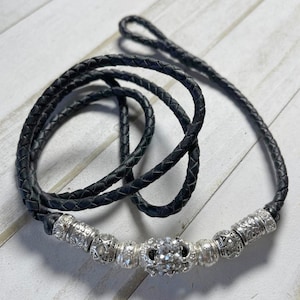 May include: A black braided leather lanyard with a silver charm featuring a large rhinestone and smaller decorative beads.