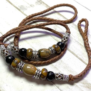May include: A brown leather cord necklace with silver metal accents and brown and black gemstone beads.