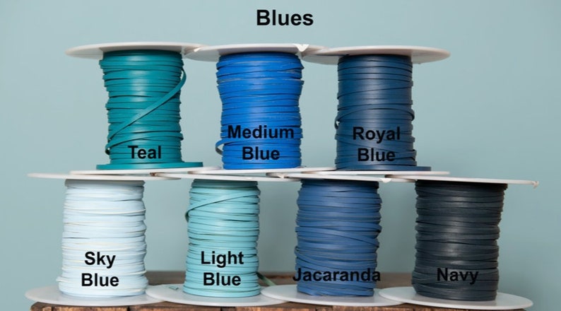 May include: Spools of leather cord in various shades of blue, including teal, sky blue, light blue, medium blue, royal blue, jacaranda, and navy. The spools are labeled with the color names.