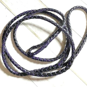May include: A braided leather cord in black and purple. The cord is approximately 3 feet long and is made of two strands of leather that are woven together.