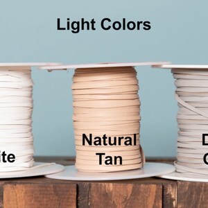 May include: Three spools of leather cord in light colors: white, natural tan, and dove grey. The spools are labeled with the color names.