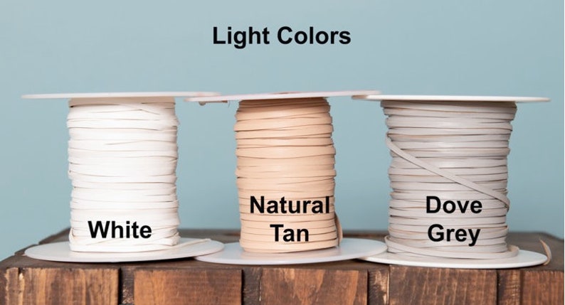 May include: Three spools of leather cord in light colors: white, natural tan, and dove grey. The spools are labeled with the color names.