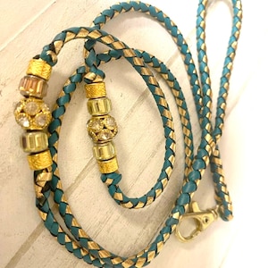 May include: A teal and gold braided leather leash with a gold clasp and two decorative beads with rhinestones.