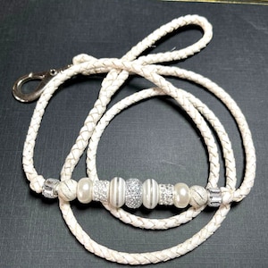 May include: White leather braided lanyard with a silver clasp and silver and white beads.