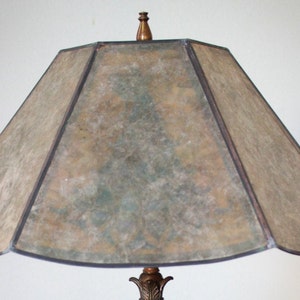 May include: A vintage lampshade with a geometric design. The shade is made of a translucent material with a mottled pattern in shades of brown, green, and beige. The shade has a black trim around the edges.