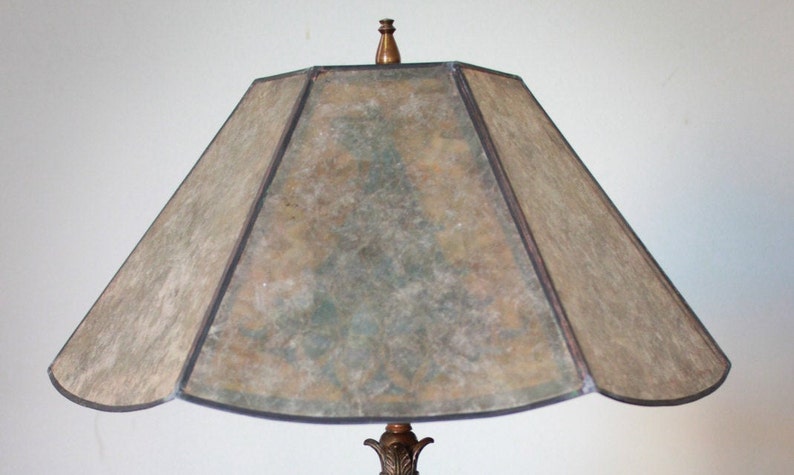 May include: A vintage lampshade with a geometric design. The shade is made of a translucent material with a mottled pattern in shades of brown, green, and beige. The shade has a black trim around the edges.