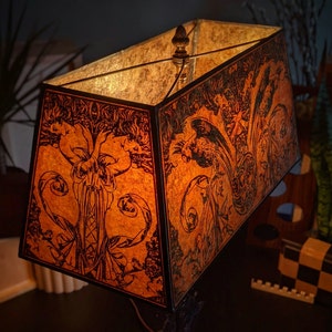 May include: A rectangular lampshade with a black frame and an orange and brown floral design. The lampshade is lit from within, casting a warm glow.