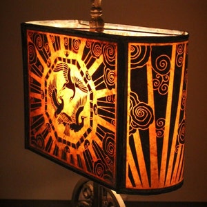May include: A lampshade with a geometric design featuring stylized birds and clouds. The lampshade is made of a translucent material and is illuminated from within, creating a warm glow.