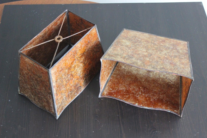 May include: Two brown lampshades with a textured surface. The lampshades are rectangular and have a black trim. One lampshade has a metal frame inside.