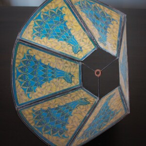 May include: A hexagonal lampshade with a geometric design featuring peacocks in shades of blue, green, and yellow on a white background.