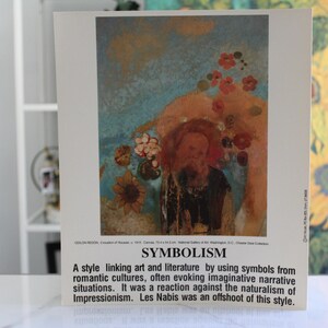 May include: A print of a painting titled "Symbolism" featuring a figure with a halo, flowers, and sunflowers. The artwork has a blue and orange color scheme. Text at the bottom describes the art style.
