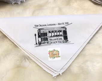 May include: White cotton handkerchief with black embroidery of a streetcar with the text "New Orleans, Louisiana - May 18, 2019" and "Megan & Joel".