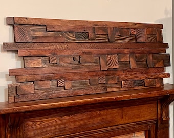May include: A rustic wooden wall art piece made from reclaimed wood. The wood is arranged in a random pattern and has a natural, weathered look. The piece is mounted on a wall above a fireplace.