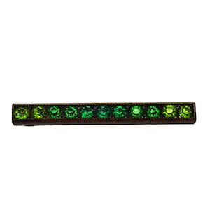 May include: A rectangular bar pin with a row of green gemstones. The gemstones graduate in color from light to dark green. The pin has a dark, possibly antique, metal setting.