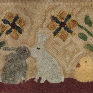 Op de afbeelding: Een vloerkleed met een bruine, witte en grijze konijn, een geel kuiken en twee gele bloemen met blauwe centra.