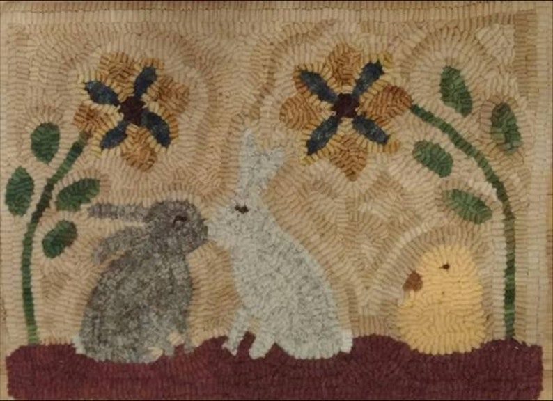 May include: A rug hooking with a brown, white, and gray bunny, a yellow chick, and two yellow flowers with blue centers.