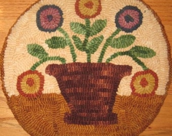 Könnte beinhalten: Ein handgestickter Teppich, der einen braunen Blumentopf mit drei Blumen darstellt. Die Blumen sind gelb, lila und rosa. Der Teppich ist braun und cremefarben.