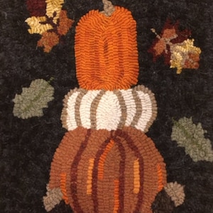 May include: A hand-stitched rug with a stack of three pumpkins. The pumpkins are orange, white, and brown. The rug is black with green and brown leaves.