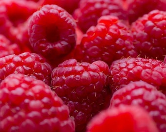May include: Close-up of a group of red raspberries. The raspberries are piled high and appear fresh and juicy.